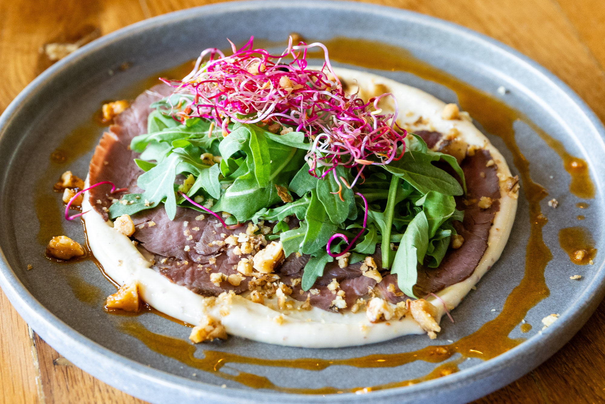 Beef carpaccio with arugula, beet sprouts and walnut crumble on cream — La Ursula